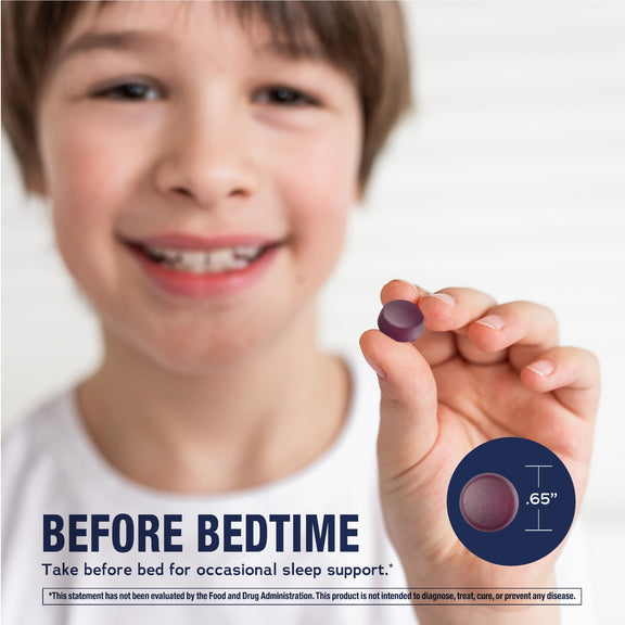 View 4 A young boy is smiling while holding a purple Kids Calm Sleep gummy in his hand.