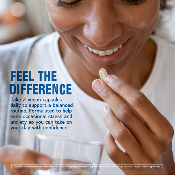 View 4 An adult woman smiles while holding an Ashwagandha capsule and a glass of water.