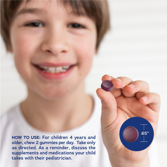 View 3 Young boy smiling, holding a 0.65-inch purple Kids Gummy. For children 4+: chew 2 daily. Consult a pediatrician.